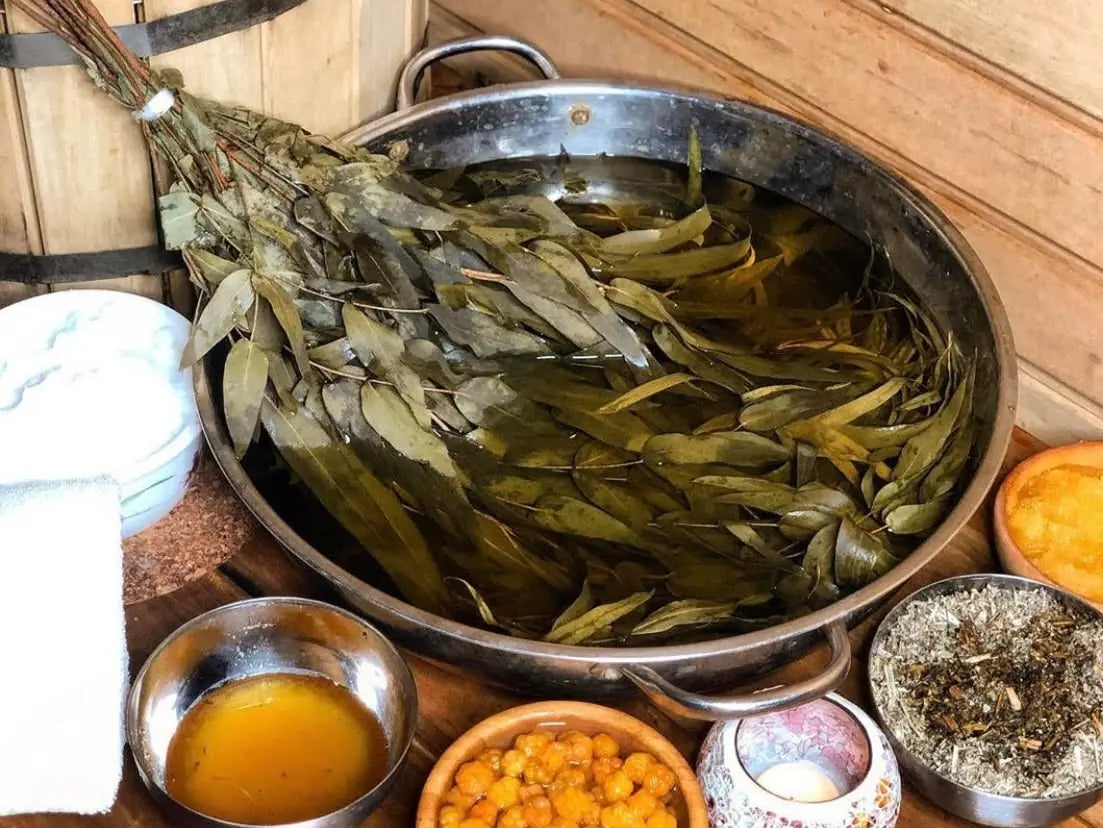 Dried natural sauna herbs and whisks soaking in a traditional wooden bucket for aromatherapy steam.
