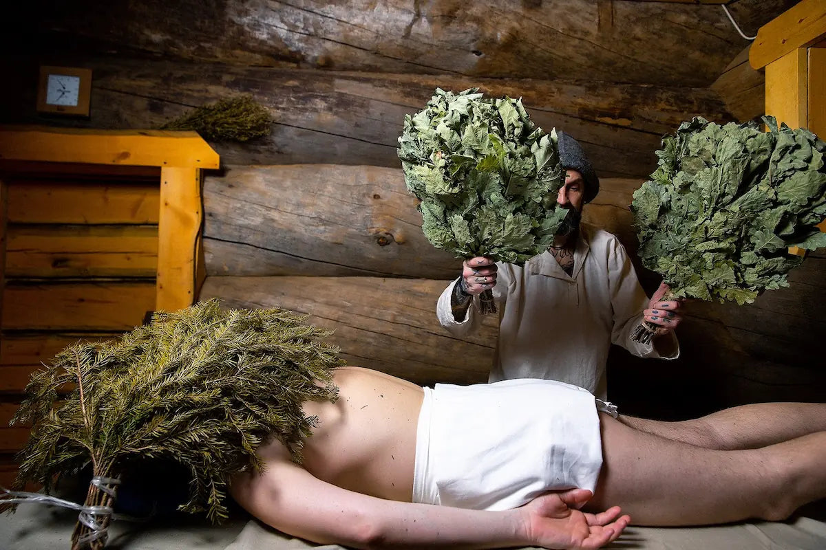 A professional sauna master performing a traditional whisking massage using oak and birch sauna whisks.